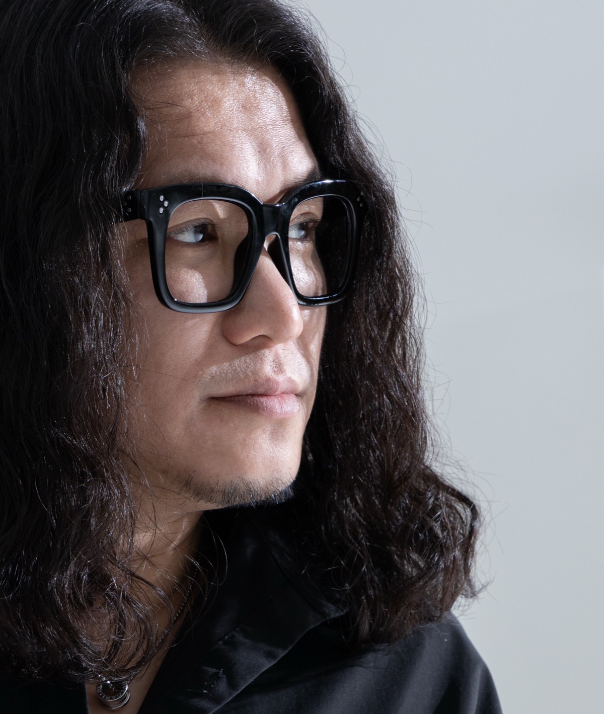 黒いシャツを着て、右のほうを見つめる華僑J。メガネをかけている。