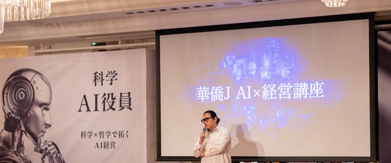 「華僑J AI×経営講座」のスクリーンと「科学 AI役員」の幕の前で、マイクを持って話す華僑J。